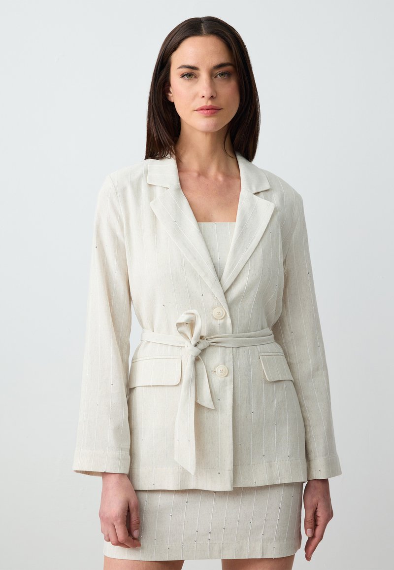 Blazer in lino beige chiaro con righe verticali, design a un bottone, due tasche frontali e cintura in tessuto. Abbinato a una gonna coordinata.