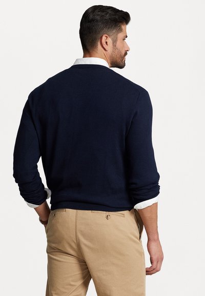 Suéter azul marino con cuello redondo, puños acanalados y una camisa blanca debajo. Con una textura suave y un corte casual.