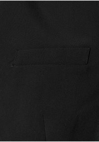 Mustaa kangasta, jossa on vaakasuora tasku, jossa on siisti ommel ja pieni ilmanvaihtoventtiili taskun alapuolella.