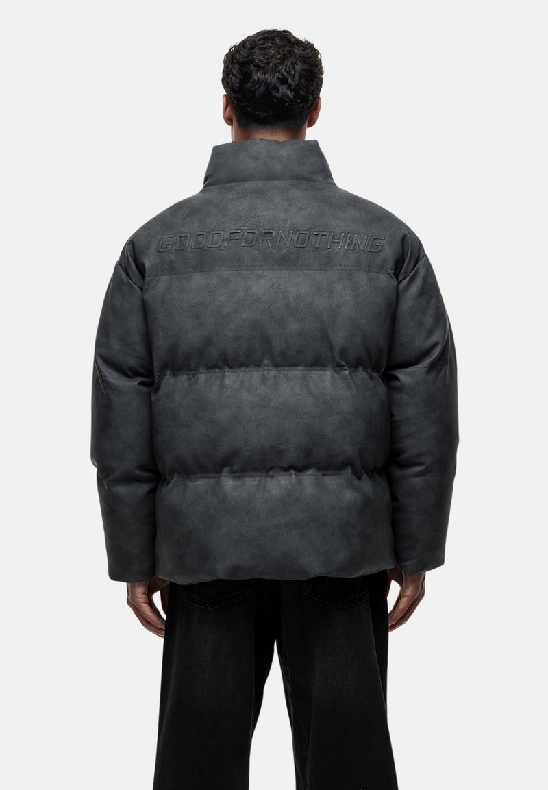 Dunkelgraue Puffjacke mit hohem Kragen, eingeprägtem Logo auf dem Rücken, gestepptem Design und elastischen Bündchen. Kombiniert mit schwarzen Hosen.