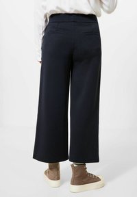 Navy wide-leg pants with side pockets, smooth texture, and a high waistband, paired with brown high-top sneakers on a white background.
