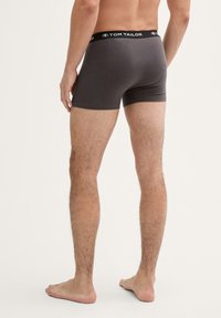 Graue Boxer Shorts aus weichem Stoff, mit einem schwarzen Bund und dem "TOM TAILOR"-Logo, enganliegend und mit einer Länge bis zur Mitte des Oberschenkels.