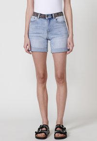 Shorts en denim bleu clair avec des revers, dotés d'une ceinture noire à motif. Le design comprend des poches avant et une fermeture éclair.