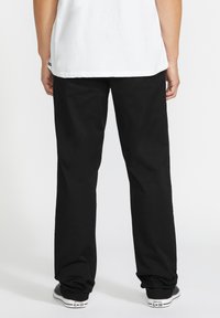 Black trousers made of sturdy fabric, featuring a straight-leg design, and worn with a white shirt and black sneakers.