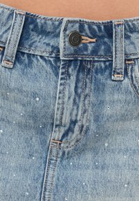 Ανοιχτό μπλε τζιν σορτς με κλασικό σχέδιο πέντε τσεπών, διαθέτει μαύρο κουμπί κλεισίματος, ξεθωριασμένη υφή και μικρές διακοσμητικές λευκές χάντρες.