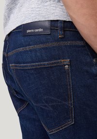 Donkerblauwe denim jeans met gele stiksel, voorzien van een merkpunt op de tailleband en een subtiel ontwerp op de achterzak.