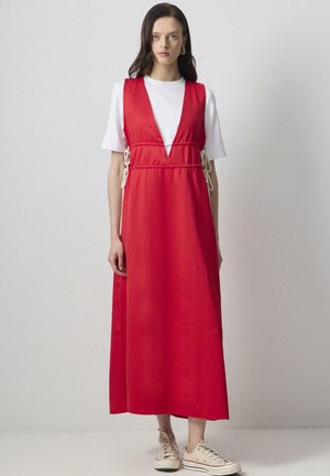 Rød maxikjole med dyb V-hals, indsnøring i taljen med hvid snor, parret med en hvid T-shirt og beige sneakers. Glat, letvægts stof.