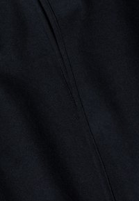 Zbliżenie na czarną tkaninę z pionowym szwem biegnącym przez środek, ukazujące strukturę i szczegóły ściegów.