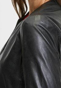 Giacca in pelle nera con texture liscia, spalle arrotondate e design minimalista con chiusura a zip. Aggiunge un tocco contemporaneo.