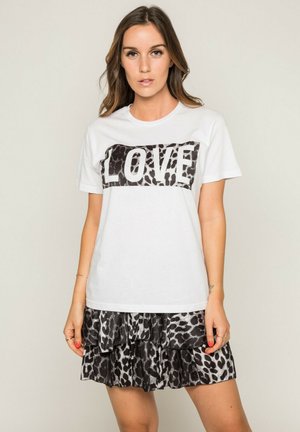 T-shirt en coton blanc avec un motif animal noir et blanc "LOVE" sur la poitrine. Associé à une jupe à volants en imprimé léopard noir et blanc.