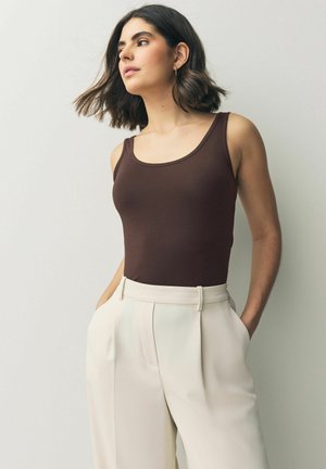 Un débardeur marron sans manches associé à un pantalon taille haute beige clair. Tissu lisse avec une silhouette ajustée et une texture subtile.