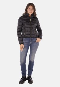 Giacca a vento nera con texture trapuntata, chiusura con zip e due tasche anteriori. Abbinata a jeans blu e stivaletti neri.