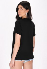 Tricou negru cu mânecă scurtă, cu un croi lejer, textură netedă și mâneci rulate, asortat cu pantaloni scurți din denim.