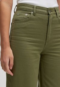 Olijfgroene katoenmix broek met een aansluitend ontwerp, ritssluiting en voorzakken. Voorzien van hardware in zilverkleur en zichtbare stikseldetails.