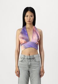 Wrap-stil halterneck-top i gradientnyanser av lila och persika, med en djup V-ringning och mjuk tyg; kombinerat med högmidjade ljusgrå jeans.