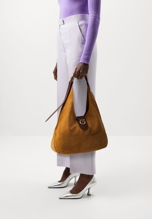 Hobo-tas van mosterdkleurig suède met een bruine leren riem en goudkleurige details. Gecombineerd met lavendelkleurige broek en zilveren hoge hakken.