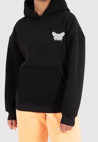 Felpa nera con tasca frontale, caratterizzata da un design di farfalla floreale bianca. Realizzata in tessuto morbido, include un cappuccio con cordino e polsini a costine.