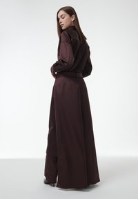 Bruine satijnen lange jurk met een kraag, lange mouwen en een ceintuur in de taille. Gladde textuur en vloeiende silhouet.