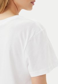 T-shirt bianco in cotone con collo rotondo e maniche corte. Tessuto liscio con cuciture sottili sulle spalle e sugli orli delle maniche.