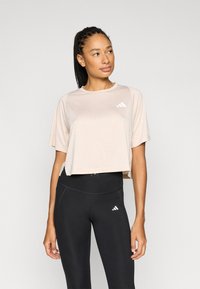 Jasnoróżowy, krótki t-shirt z krótkimi rękawami i białym logo Adidas; w połączeniu z czarnymi, dopasowanymi legginsami z podobnym logo.