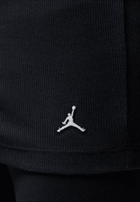 Zwarte atletische short met geribbelde textuur, voorzien van een wit geborduurd Jumpman-logo op de linkerzoom. Simpel design, knielengte.