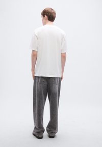 Λευκό μπλουζάκι με κοντά μανίκια συνδυασμένο με φαρδιά, ξεθωριασμένα γκρι τζιν. Απλός σχεδιασμός με χαλαρή σιλουέτα.