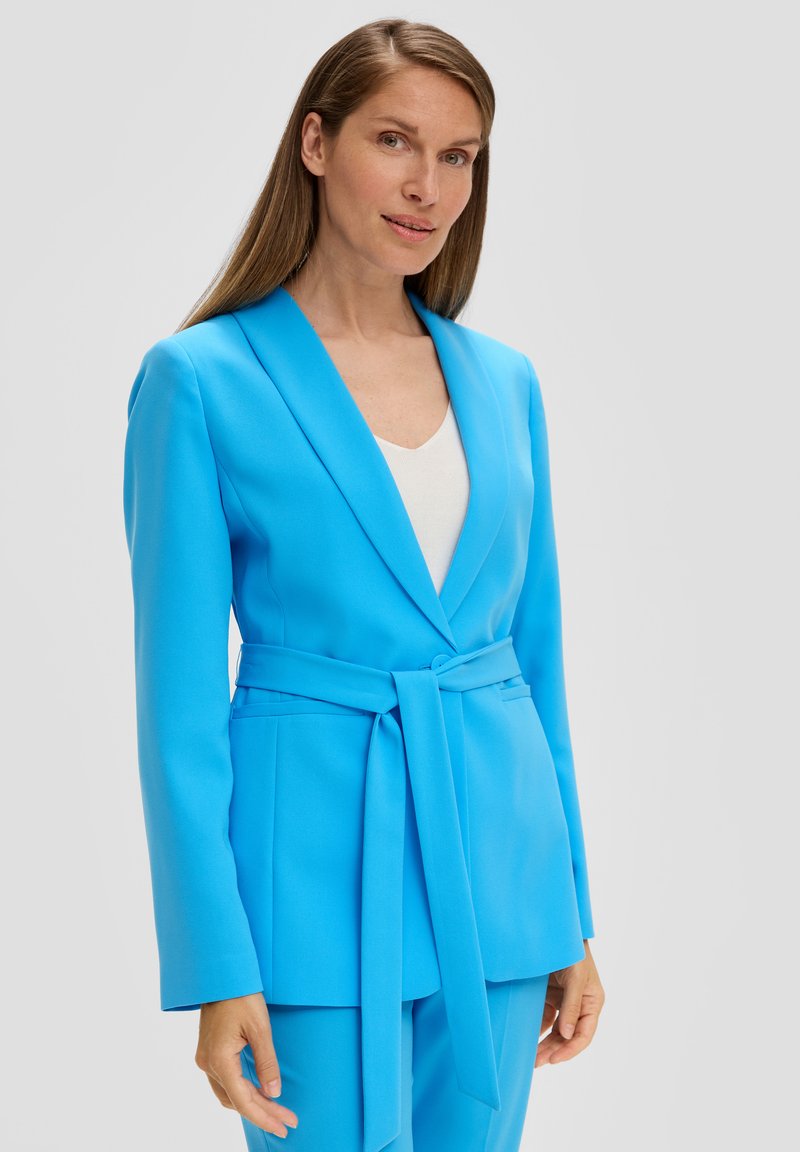 Blazer ajusté bleu vif avec un revers cranté, des manches longues, et une large ceinture, complété par un pantalon assorti. Texture lisse.