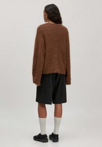 Bruine harige brei-sweater met een ontspannen pasvorm, gecombineerd met zwarte shorts tot de knie en witte kniekousen, gedragen met zwarte schoenen.