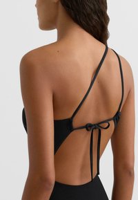 Čierny horný diel bikín s krížovým zadným dizajnom, nastaviteľnými šnúrkami a hladkou textúrou látky. Minimalistický štýl bez ďalších vzorov.