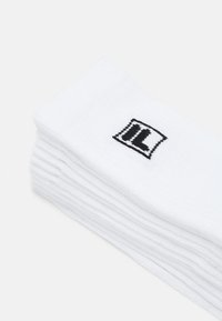 Vita bomullssockor staplade prydligt, med en svart broderad logotyp på ena sidan, med ribbad textur och mjuk yta.