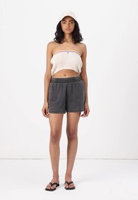Crop top côtelé beige clair avec des accents violets, porté avec un short ample gris foncé et des sandales noires. Design simple, coupe décontractée.