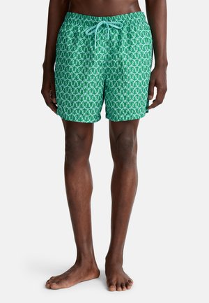 Grüne Schwimmshorts mit Muster und Kordelzugbund, die ein geometrisches Design in verschiedenen Grüntönen und Weiß zeigen.