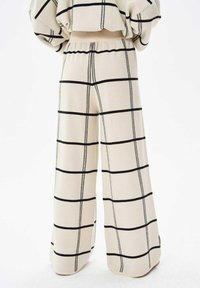 Wijduitlopende broek in een crèmekleurige stof met een zwart ruitpatroon. Elastische tailleband, zachte textuur, geen zichtbare sluitingen of zakken.