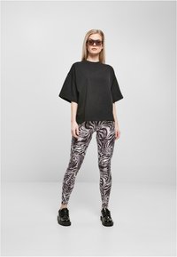 Čierne oversized tričko v kombinácii so legínami so zebrovým vzorom v odtieňoch šedej a bielej, doplnené čiernymi šnurovacími topánkami a slnečnými okuliarmi.