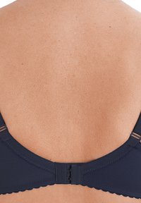 Reggiseno blu navy con tessuto liscio, bordi ondulati, spalline regolabili e chiusura con gancetto sul retro, che mostra il tono della pelle.