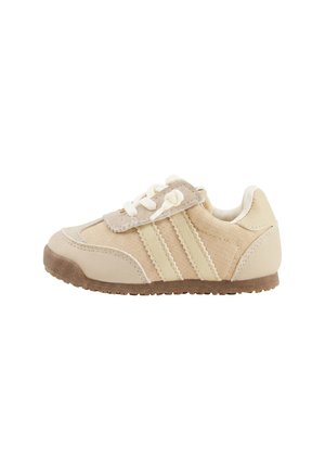 Beige-hellcremefarbener Turnschuh für Kleinkinder mit zwei Klettverschlüssen, Schnürdetail und strukturiertem braunem Gummisohlen, seitlich auf weißem Hintergrund betrachtet.