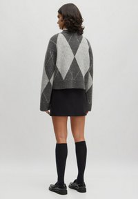 Grau und schwarz kariertes cropped Sweatshirt aus Wollmischung mit geripptem Saum, kombiniert mit einem schwarzen Rock und knielangen Socken, die einen geschichteten Look erzeugen.