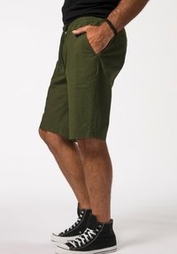 Olivgrüne Shorts mit einem elastischen Bund und Kordeln, Seitentaschen und geradem Schnitt. Getragen mit schwarzen High-Top-Sneakern.