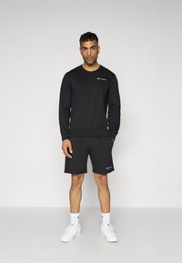 Black sweatshirt and shorts made of soft cotton blend, featuring embroidered logo accents. Model wears white sneakers and socks.