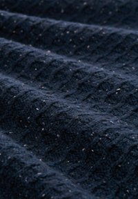 Marineblauw textiel met een verheven diamantpatroon, voorzien van vlekken in wit en lichter blauw, met een zachte, geweven uitstraling.