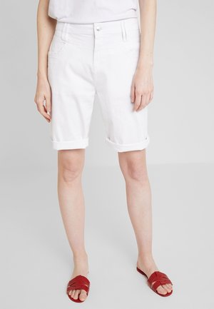 Shorts en denim blancs avec une coupe droite, un ourlet retroussé, des poches avant et une fermeture à bouton en métal. Portés avec des sandales plates rouges.