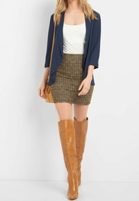 Námořnický sako přes bílý top, doplněný texturovanou hnědou mini sukní s vzorem a hnědými koženými kozačkami po kolena. Malá světle hnědá kabelka.