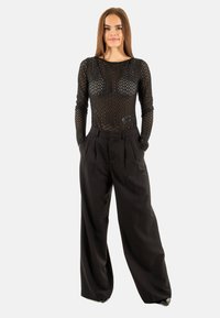 Maglietta nera a maniche lunghe con un motivo testurizzato, abbinata a pantaloni neri a vita alta e a gamba larga, creando una silhouette aderente ma rilassata.