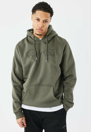 Hoodie vert olive avec une poche avant, des cordons de serrage et un logo "Project Paris" brodé. Tissu doux et coupe décontractée. Superposé avec une chemise blanche.