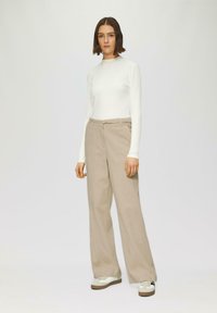 Haut blanc côtelé à manches longues associé à un pantalon large beige. Les baskets présentent un design crème et noir avec une semelle marron.