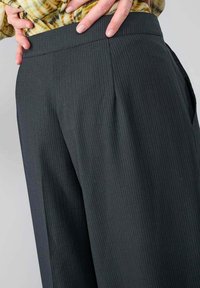 Weit geschnittene Hosen in Dunkelgrau mit feinen vertikalen Streifen. Aus einem leichten Stoff gefertigt, mit einem glatten Bund und seitlichen Taschen.