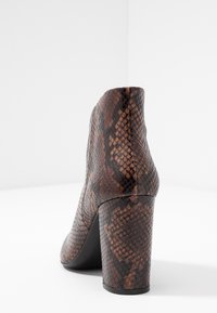 Brązowy botek za kostkę w motyw zwężających się nadruków węża, z teksturowaną skórzaną powierzchnią, zwężanym wysokim obcasem i gładką czarną podeszwą.