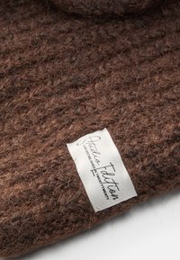 Brun strikket tekstil med en grov tekstur, med en hvit etikett merket "Studio Edition" sydd langs kanten.