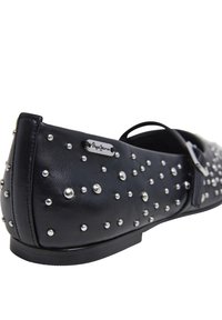 Français : Chaussure plate en cuir noir avec des clous en argent, des fines lanières et une plaque de logo en métal. Le design est plat avec un bout rond et un talon minimal.