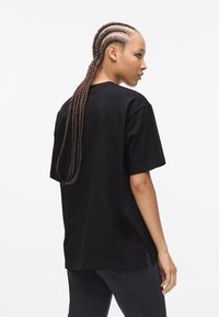 Svart oversized T-skjorte med korte ermer, laget av bomull. Har en avslappet passform og sidespalter i falden. Enkelt design uten mønstre.